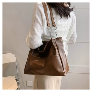 Detailed view of brown tote bag with front pocket and decorative silver chain strap detail