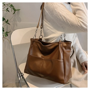 Close-up of brown tote bag with metal chain strap and dual front pocket detail