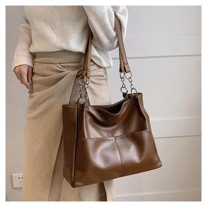 Fashionable dark brown large tote bag with silver chain handles worn by a model