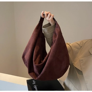 Detail of burgundy suede hobo bag carried by a model in a minimalist urban setting