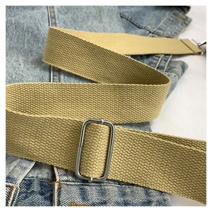 Close-up of thick khaki canvas shoulder strap with silver metal buckles on denim background