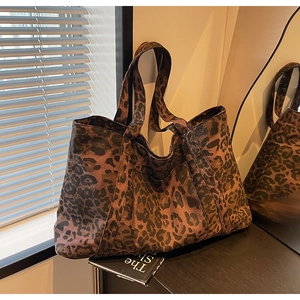 Close-up detail of leopard print tote bag with wide shoulder strap in warm indoor lighting