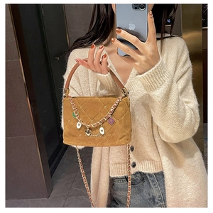 Brown suede quilted handbag with heart charms and metal chain strap held by model