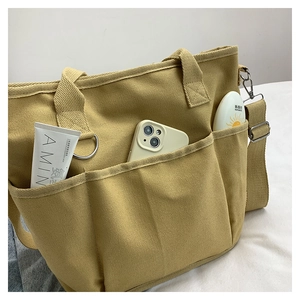 Detail of yellow canvas tote bag with front pockets showing storage for phone and cosmetics