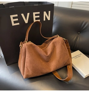 Detail of a brown suede hobo bag with gold hardware placed on a black leather sofa