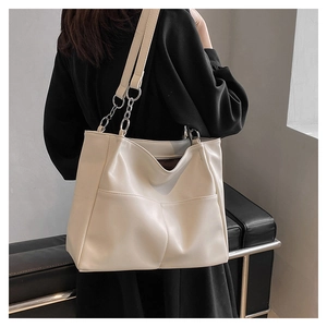 Detail view of cream tote bag featuring front pockets and silver chain leather strap