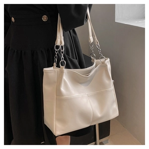 Close-up of a large beige tote bag featuring silver chain straps and front pockets