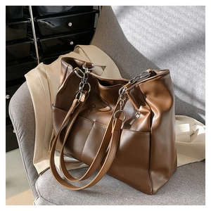 Detail view of brown faux leather tote with silver chain and stitched texture on a chair