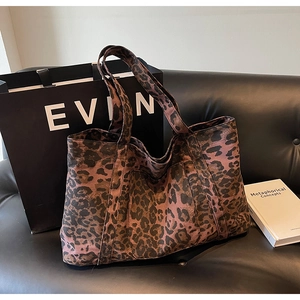 Detail of leopard print tote bag with reinforced handles on a black leather sofa