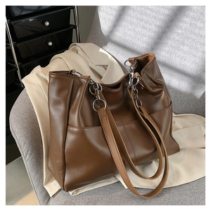 Detail view of a brown tote bag with silver chain straps shown on a stylish sofa