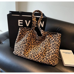 Detailed view of leopard print tote bag placed on black leather sofa in a modern setting