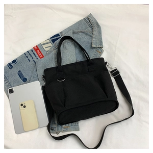 Detail view of black canvas tote bag with adjustable strap and front pocket storage