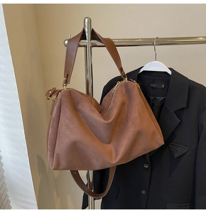 Detail of a large brown suede tote bag with metal zipper and wide shoulder strap