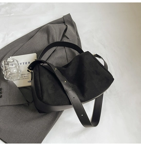 Detail of black suede hobo bag with smooth leather strap and metal buckle on grey blazer
