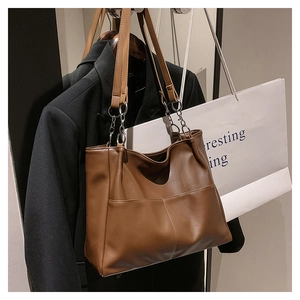 Detail view of large brown leather tote bag with silver chain straps and side pockets