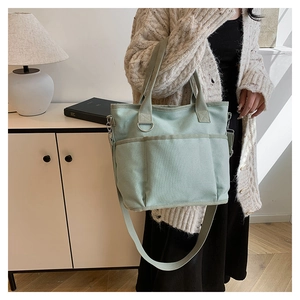 Detail view of mint green canvas tote bag with three front pockets and crossbody strap