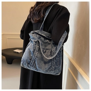 Model wearing a large washed blue denim tote bag with side zipper and versatile straps