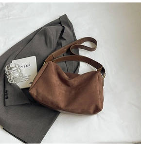 Detail shot of brown suede shoulder bag resting on a grey blazer with stylish art props