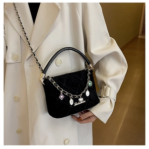 Elegant black quilted crossbody bag with gold chain and handle shown on beige coat