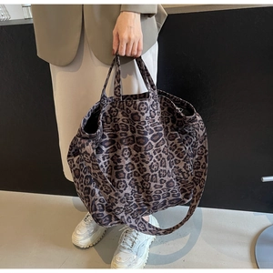 Detail of leopard print tote bag with dual handles and long shoulder strap worn by model