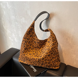 Détail d'un sac hobo léopard avec anse en cuir noir posé sur un canapé élégant