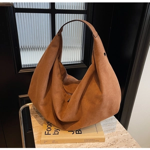 Brown suede hobo shoulder bag with minimalist design placed on a book over stone surface