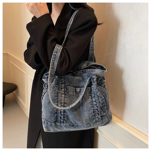Detail of blue washed denim tote bag showing fabric texture and metal buckle on the pocket