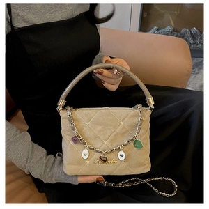 Close-up of quilted beige handbag with gold chain and colorful heart-shaped charms