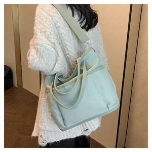 Detail showing side pocket of light green canvas tote bag on white sweater