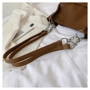 Detailed close-up of brown leather tote strap with silver chain and metal ring accents