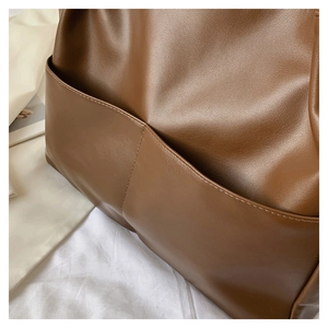 Detail of a brown leather tote bag showing large pocket structure and fine stitching