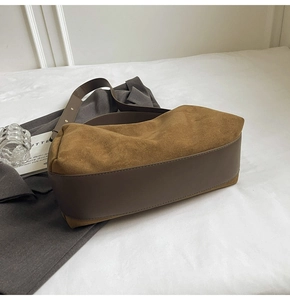 Macro detail of Earth-tone suede baguette bag with wide shoulder strap and contrast stitching