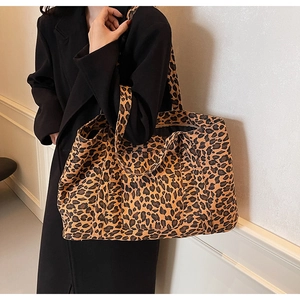 Detailed view of large leopard print tote bag with wide straps on a black coat model