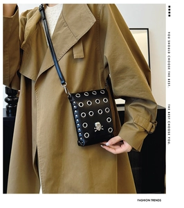 Detail of black crossbody phone bag with skull emblem and metal eyelets on model