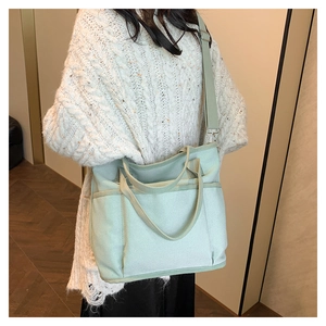 Detail of mint canvas tote bag with adjustable strap and front pocket on model