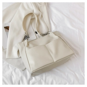 Detail of a creamy white oversized tote bag featuring silver chain straps and large pockets