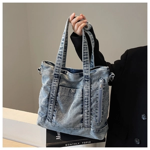 Detailed texture of a washed blue denim tote bag with heavy-duty straps and metal D-ring