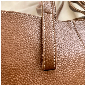 Detailed macro view of white stitching on the brown lychee grain leather tote bag strap