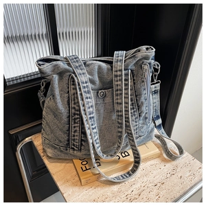 Detail view of washed blue denim tote bag with metal snap pocket and smooth zippers