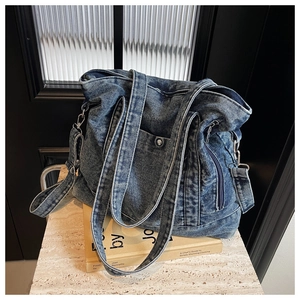 Detail of blue denim tote bag showing side pockets, zippers, and removable shoulder strap