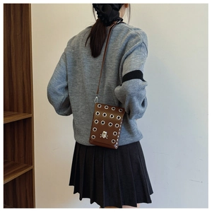 Brown leather crossbody phone bag with skull accent and silver eyelets shown on a model