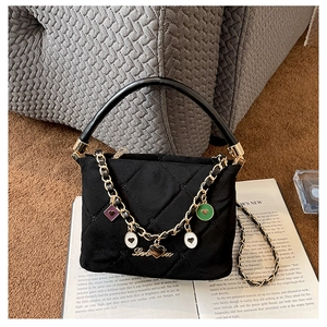 Detailed macro view of black quilted handbag with colorful heart enamel charms on gold chain