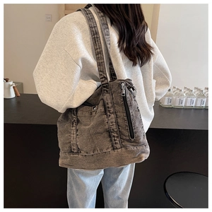 Detail view of washed grey denim tote bag with vertical zipper and metal hardware accents