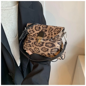 Detail of leopard print crossbody bag with metal lock and black leather strap worn by model