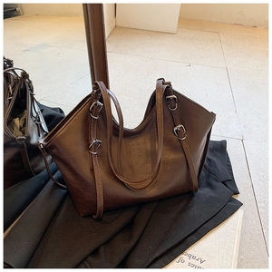 Detail of dark brown faux leather tote bag with metal buckles on black blazer backdrop