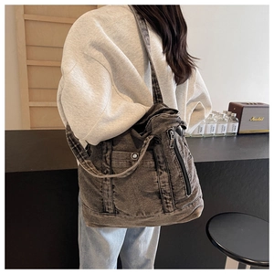 Detail view of large charcoal gray washed denim tote bag worn by a model in casual setting