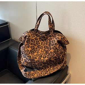 Close-up of leopard print tote bag with wide shoulder strap on a black leather sofa