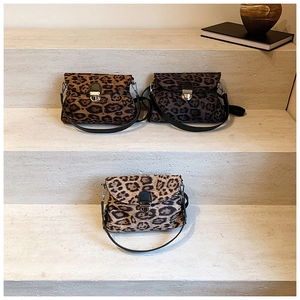 Three stylish leopard print crossbody bags with metal clasps on a modern stone staircase