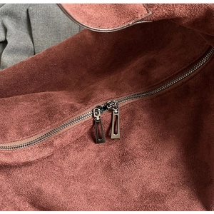 Close-up of dual metal zippers and premium suede texture on a red shoulder bag