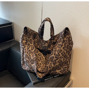 Close-up of leopard print canvas tote bag with thick shoulder strap on a black sofa